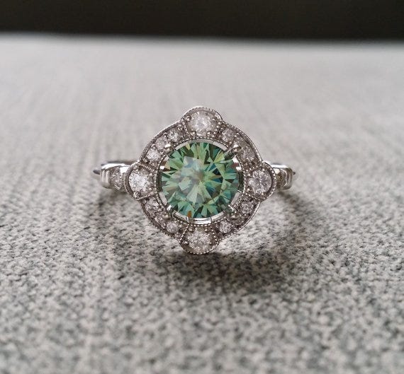 This ring from PenelliBelle on Etsy features a diamond halo and an AMAZING blue green moissanite stone